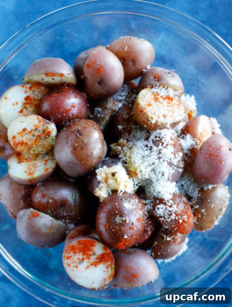 The cut potato halves coated in a vibrant mixture of spices, herbs, and parmesan cheese, ready for roasting.