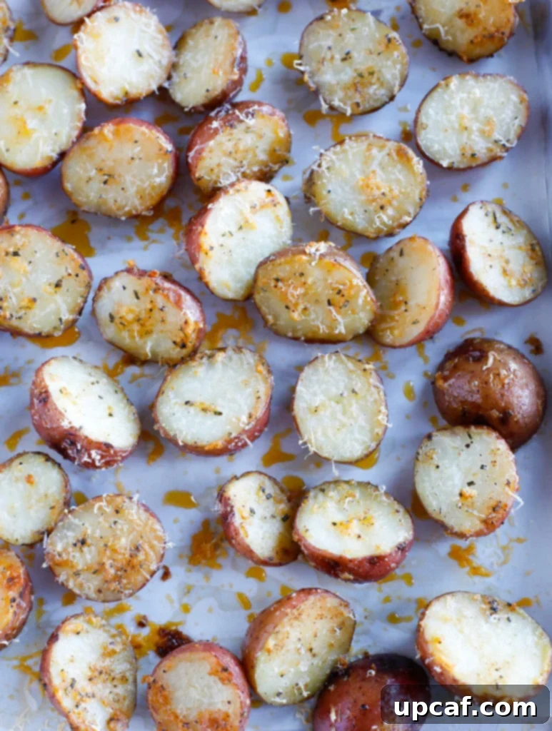 Seasoned potato halves spread out on a parchment-lined baking sheet, showing the even coating and spacing.