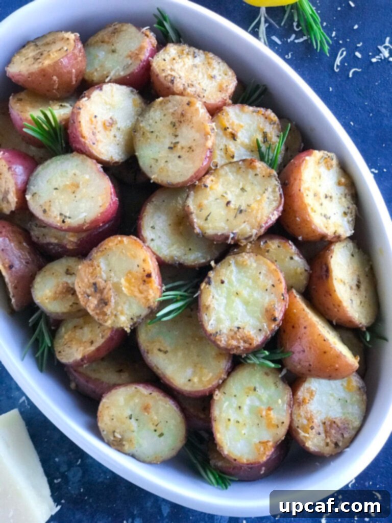 A serving of parmesan roasted potatoes garnished with fresh herbs, presented in an elegant white dish.