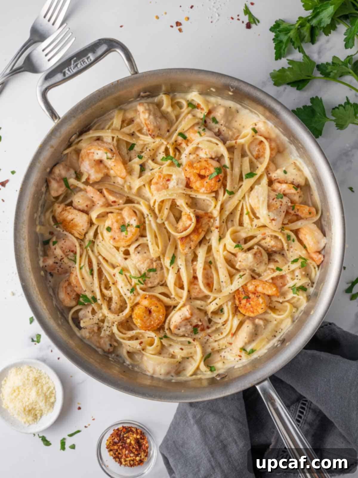 A skillet of creamy chicken and shrimp alfredo, garnished with fresh herbs.