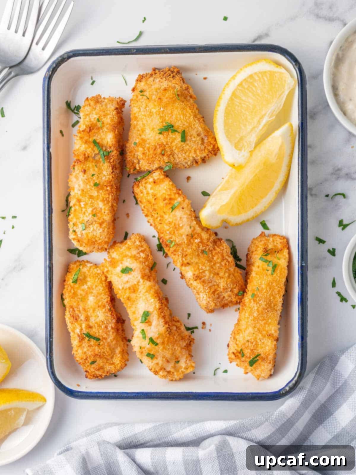 Guilt-Free Crispy Air Fryer Fish and Chips 2 A platter of crispy panko fried fish sticks with lemon wedges and parsley.