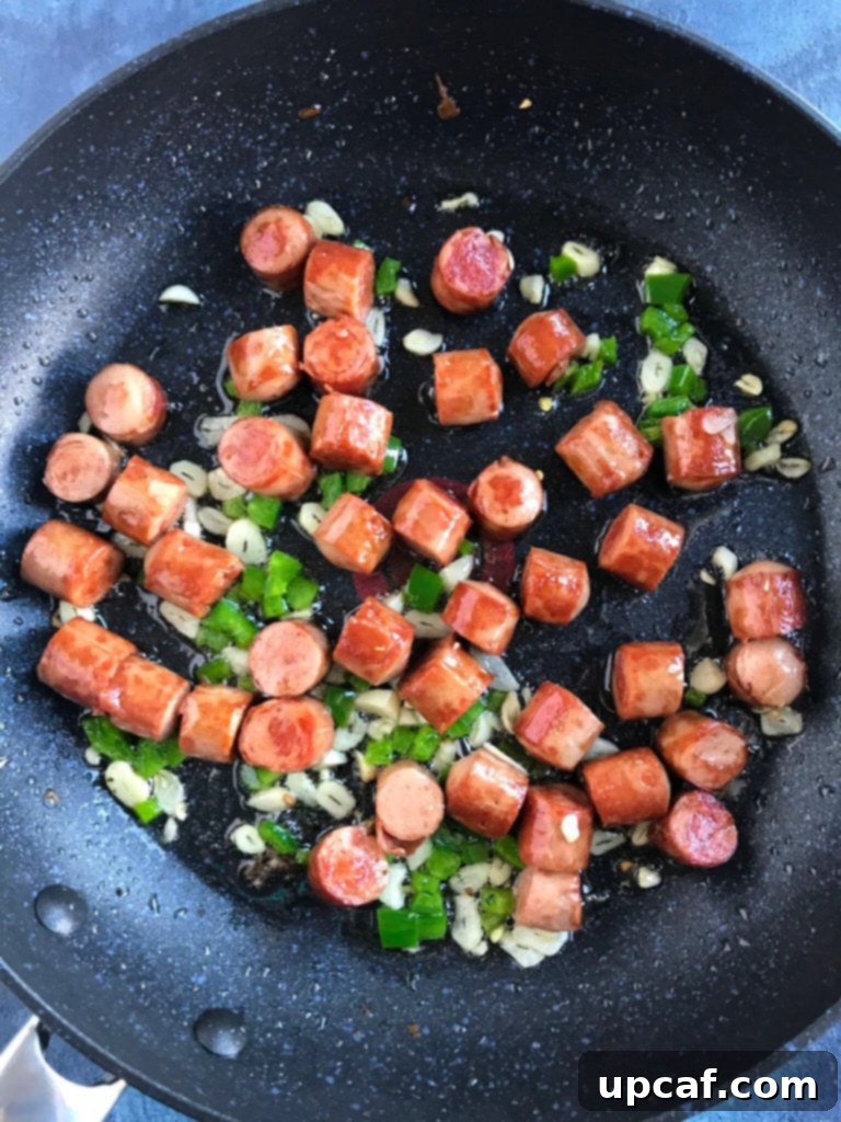Crispy sausage pieces cooking in a pan with garlic and jalapeño