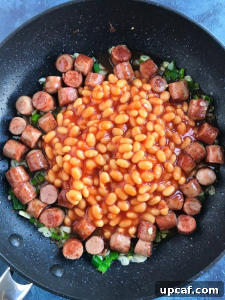 Baked beans simmering with crispy sausage and aromatics in a pan