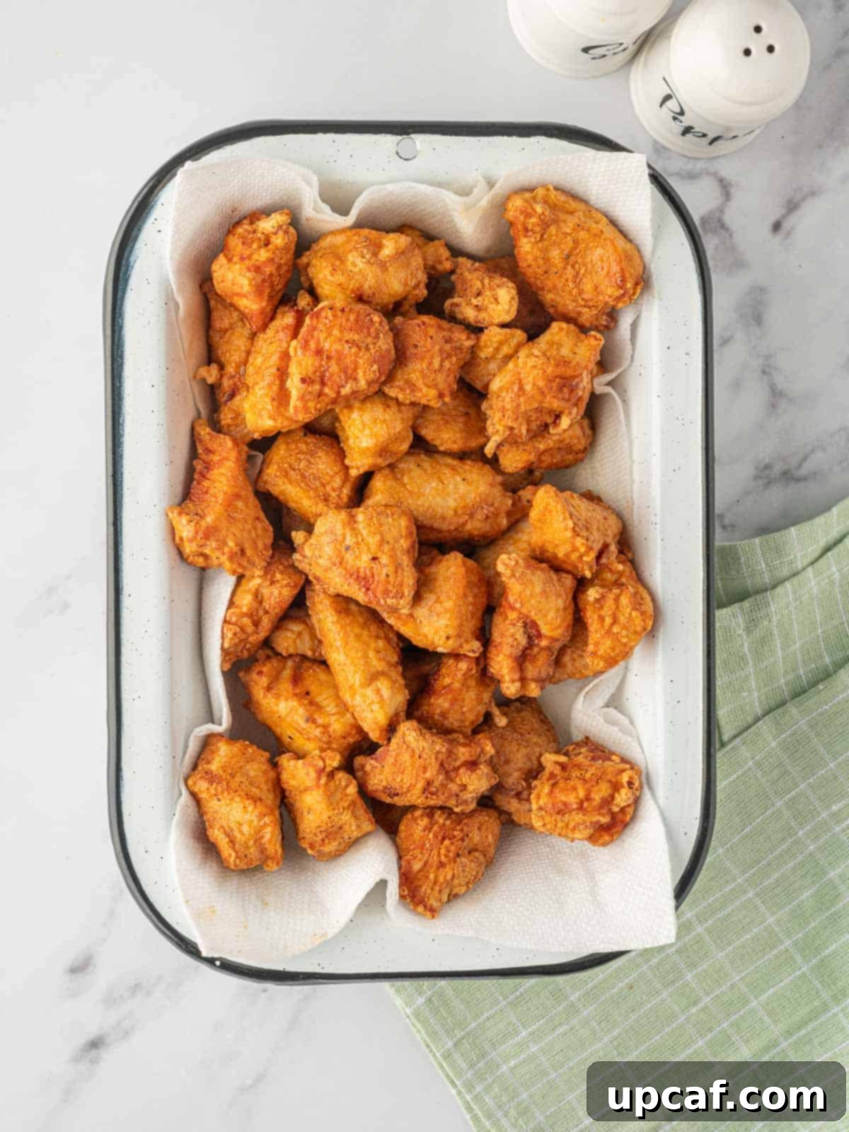 Crispy Garlic Chili Chicken 5 A close-up view of golden-brown, deep-fried crispy chicken pieces resting on paper towels, draining excess oil.