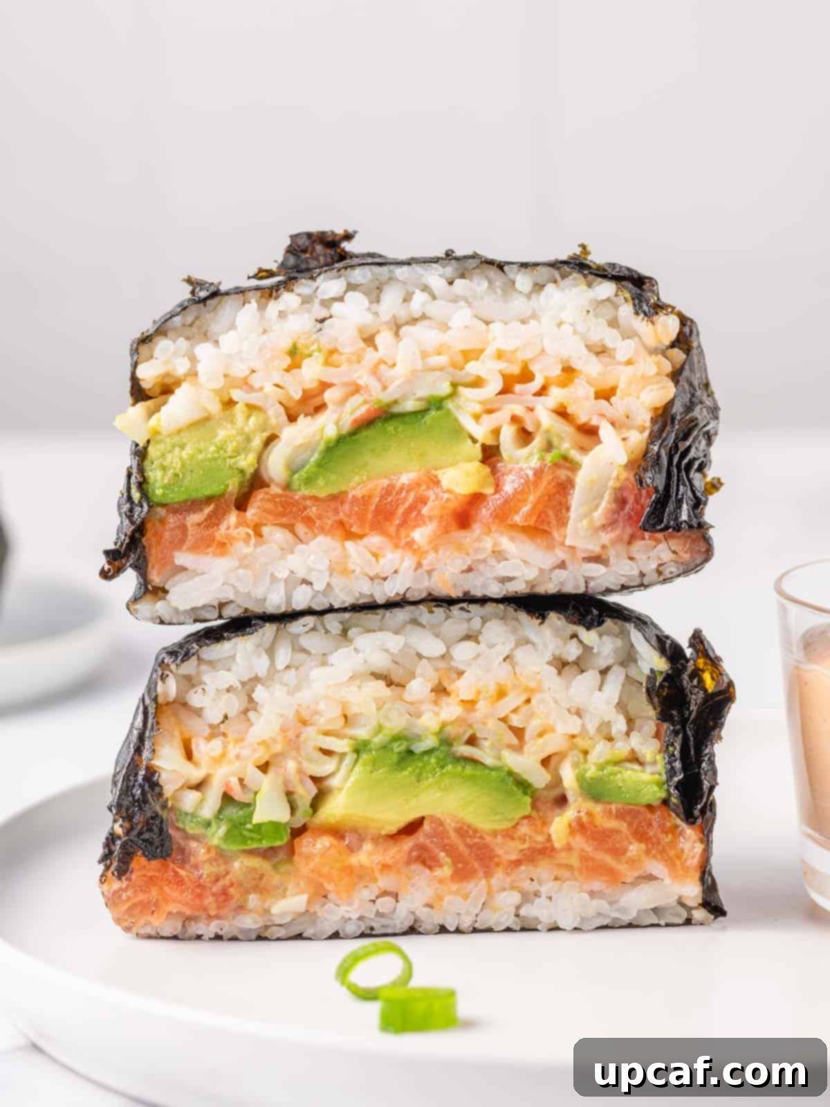 Two halves of a nori wrap sushi burger stacked on top of each other, showcasing layers of rice, salmon, avocado, and crab.