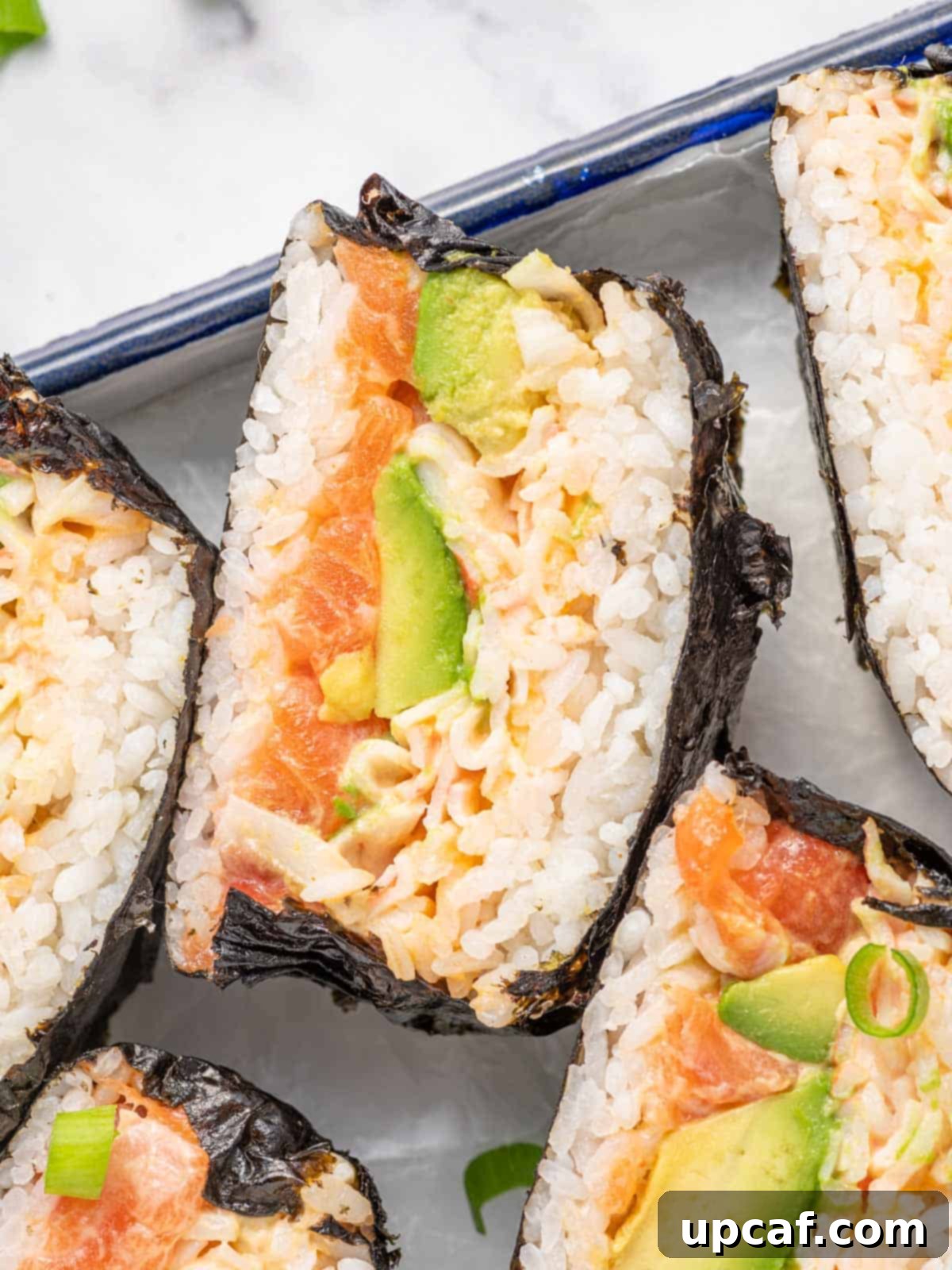 A beautifully presented sushi burger sliced in half, showcasing its intricate layers on a serving tray.