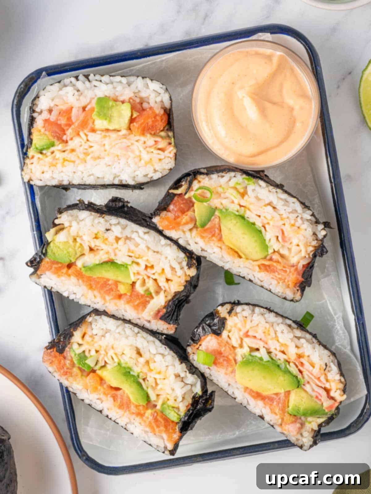 Two rice bun sushi burgers, sliced in half to reveal the layered fillings, artfully arranged on a serving tray.