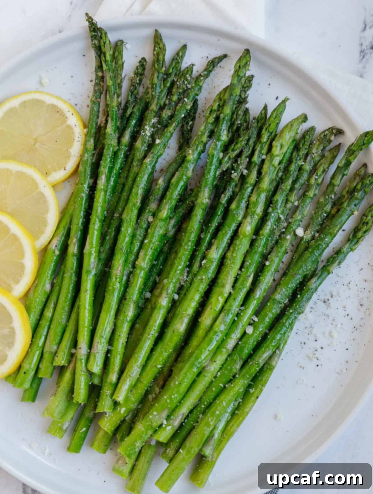 Crispy air fried asparagus on a plate, garnished with fresh herbs and lemon slices.