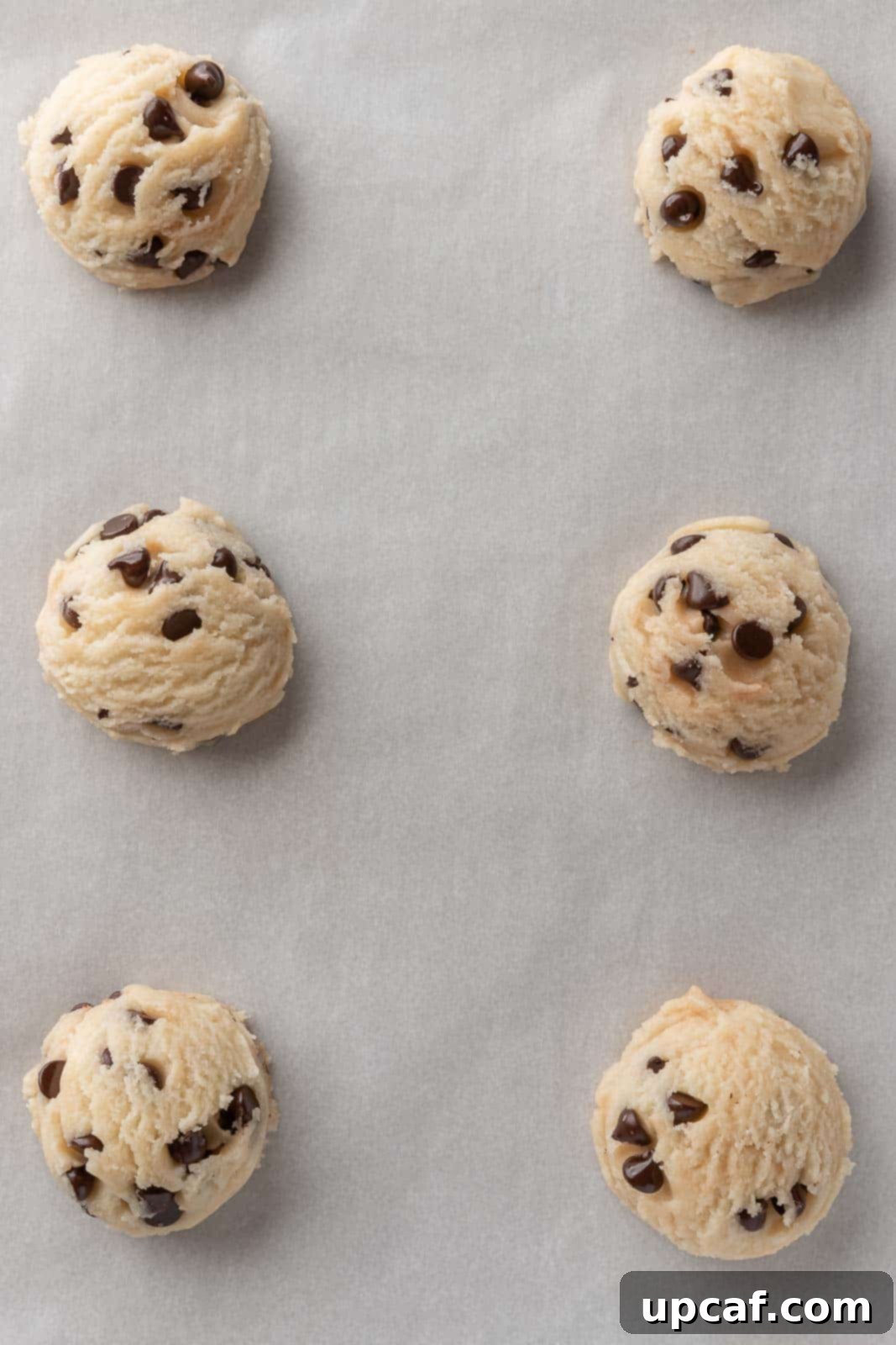 Scoops of egg-free cookie dough perfectly spaced on parchment paper on a baking sheet.