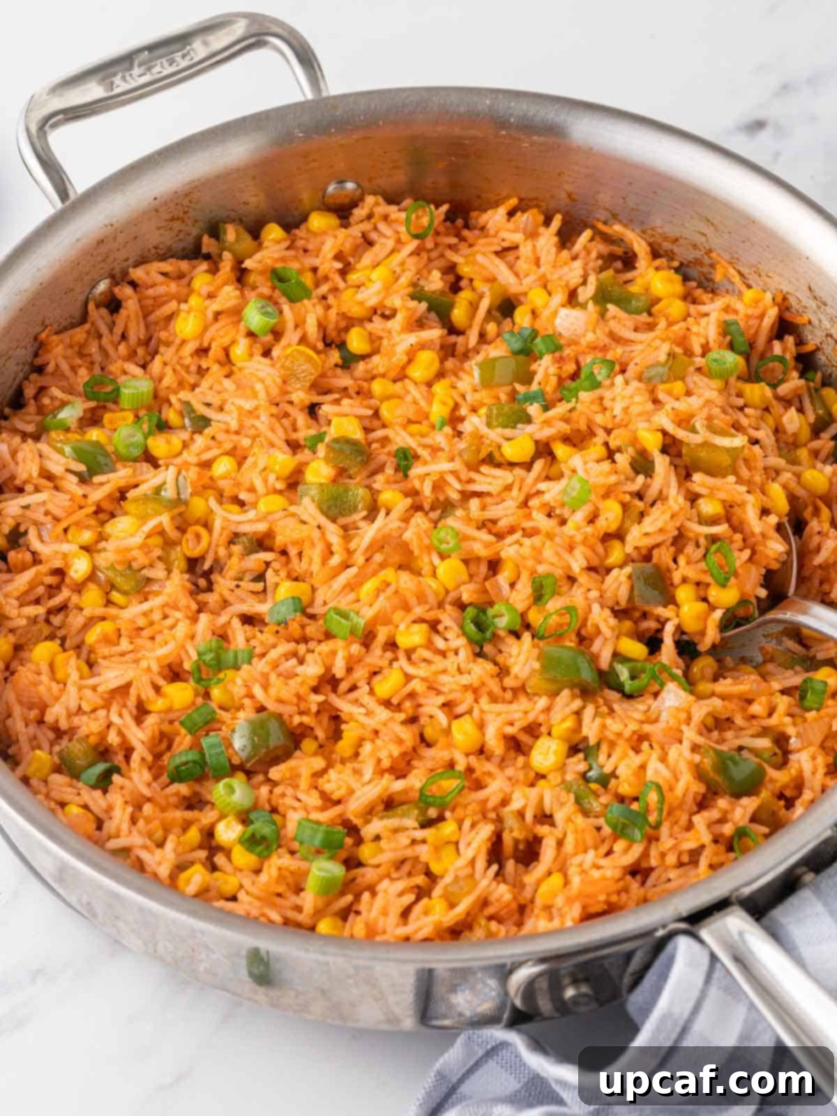 A large skillet filled with freshly made Mexican Fried Rice, with a spoon scooping a portion.