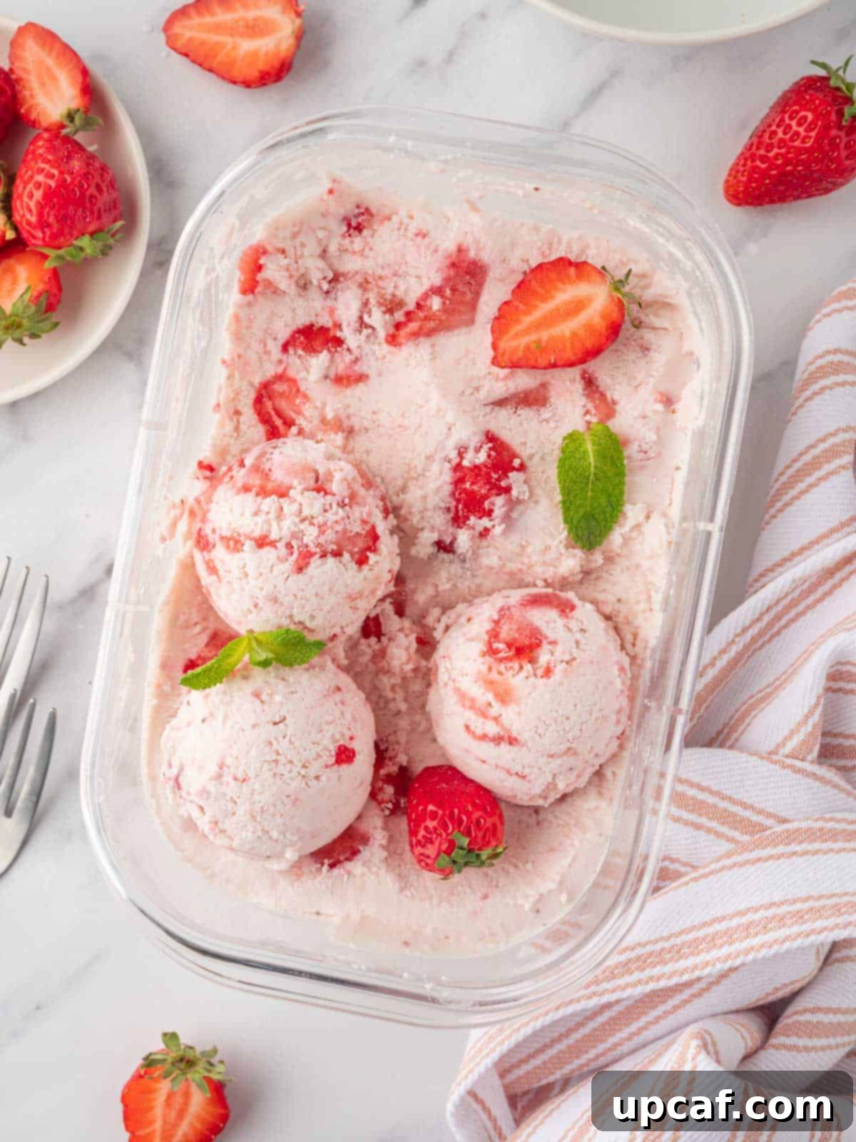 Scoops of vibrant strawberry cottage cheese ice cream in a white container, garnished with fresh strawberries.