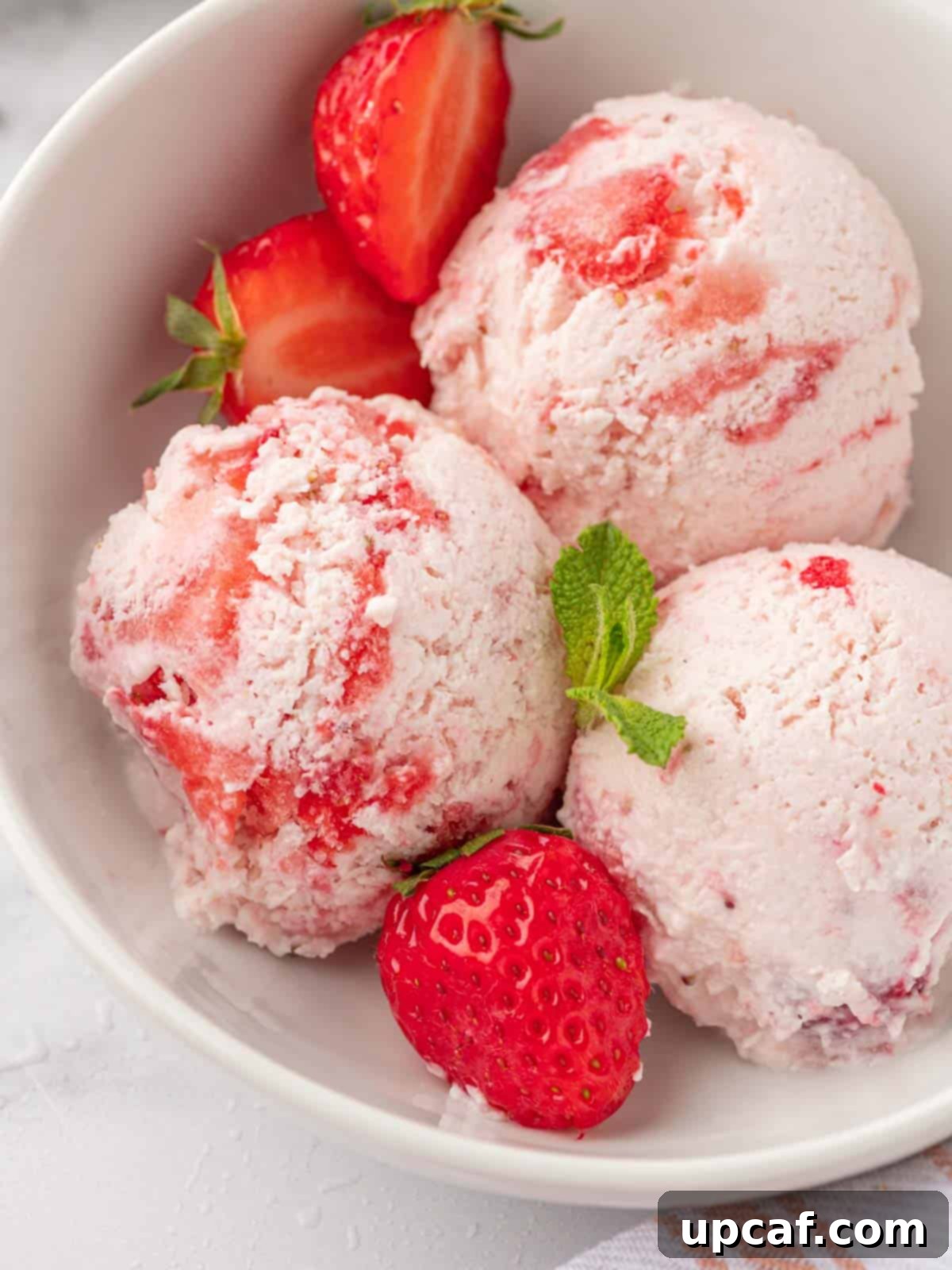 Multiple scoops of vibrant strawberry cottage cheese ice cream served in a glass bowl, garnished with fresh mint leaves and whole strawberries.