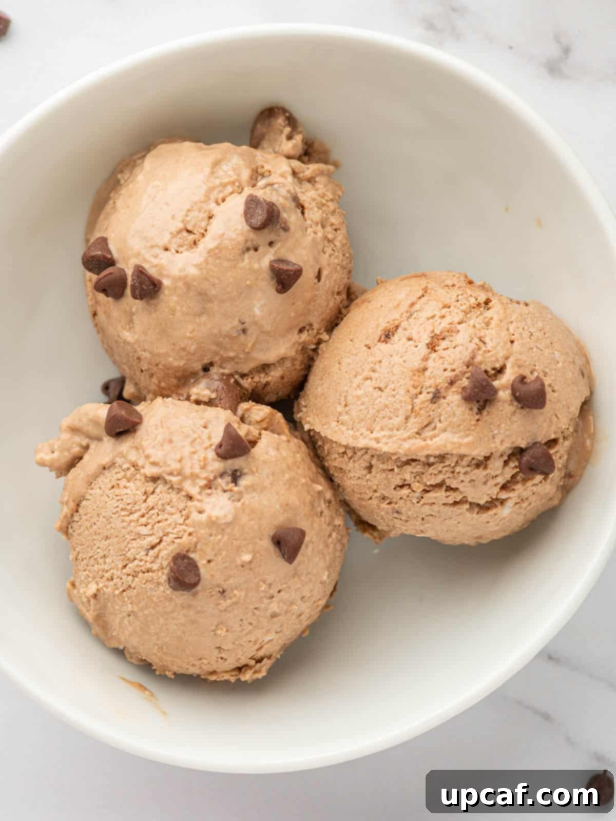 Several scoops of rich chocolate peanut butter cottage cheese ice cream in a white bowl, garnished with chocolate shavings.