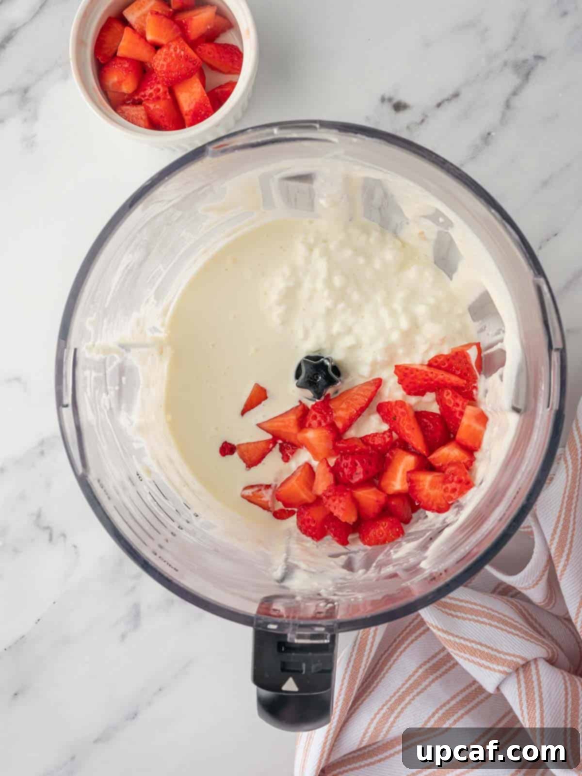 A food processor actively blending ingredients for strawberry cottage cheese ice cream, showing a swirling pink mixture.