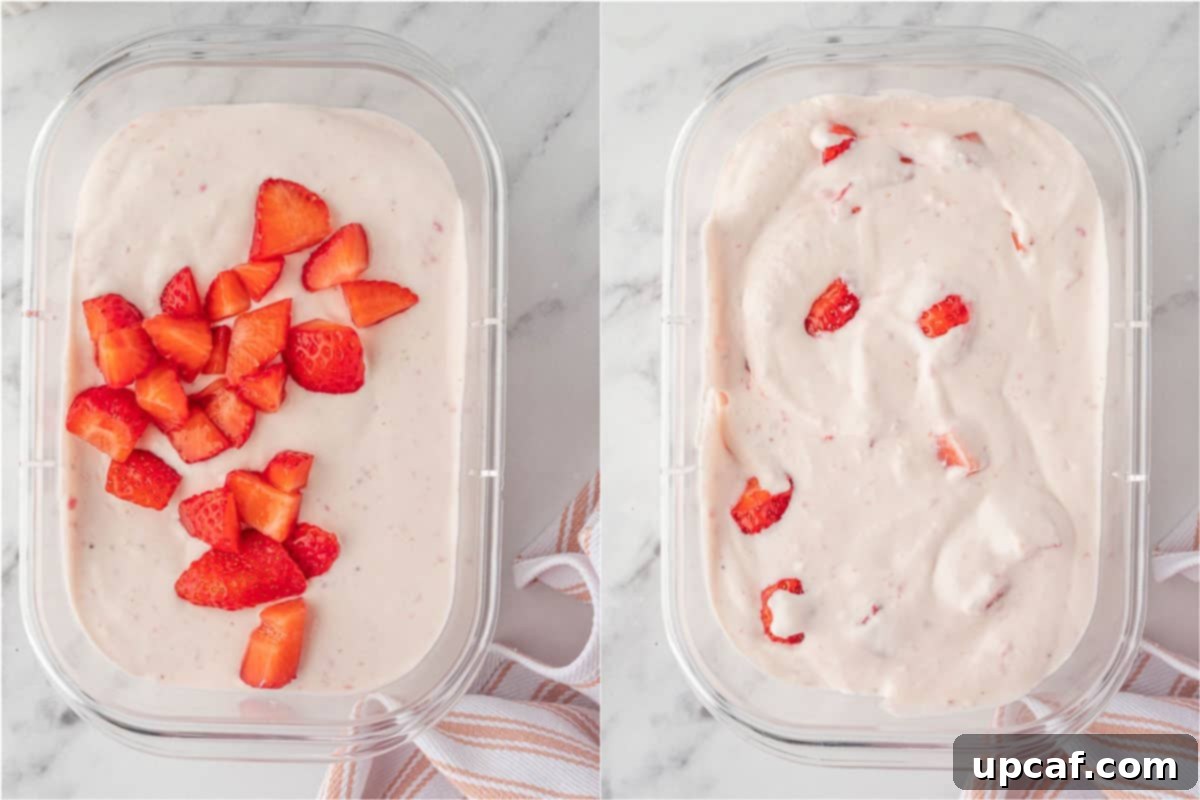Chopped strawberries being gently folded into the strawberry cottage cheese ice cream mixture in a container, preparing it for freezing.