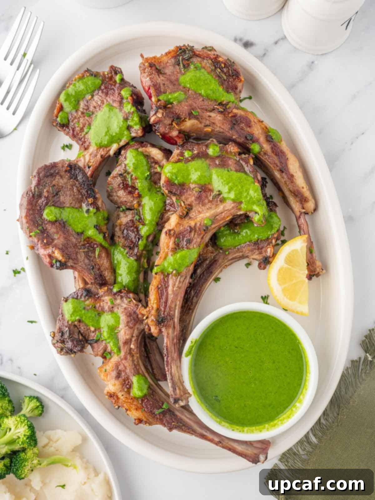 A platter of beautifully grilled Mediterranean lamb chops garnished with fresh mint and lemon, served with a vibrant mint herb sauce.