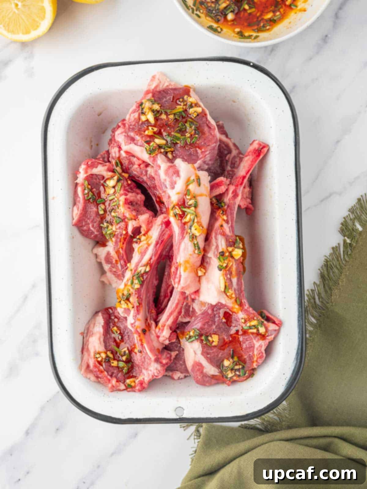Raw lamb chops soaking in a vibrant Mediterranean marinade in a bowl, ready for grilling.
