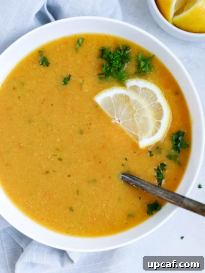 A close-up of a white bowl filled with creamy Lebanese Lentil Soup, garnished with fresh parsley and lemon, with a spoon resting in the bowl, highlighting its inviting texture.