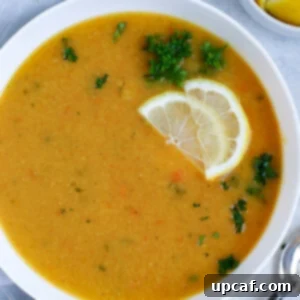 Lebanese lentil soup served in a white bowl and garnished with lemon wedges and parsley