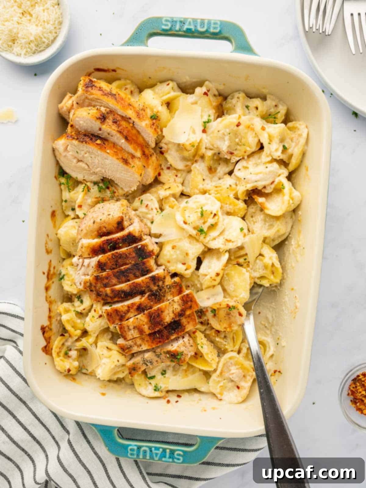 A spoon dishing out a generous serving of creamy alfredo tortellini with grilled chicken.