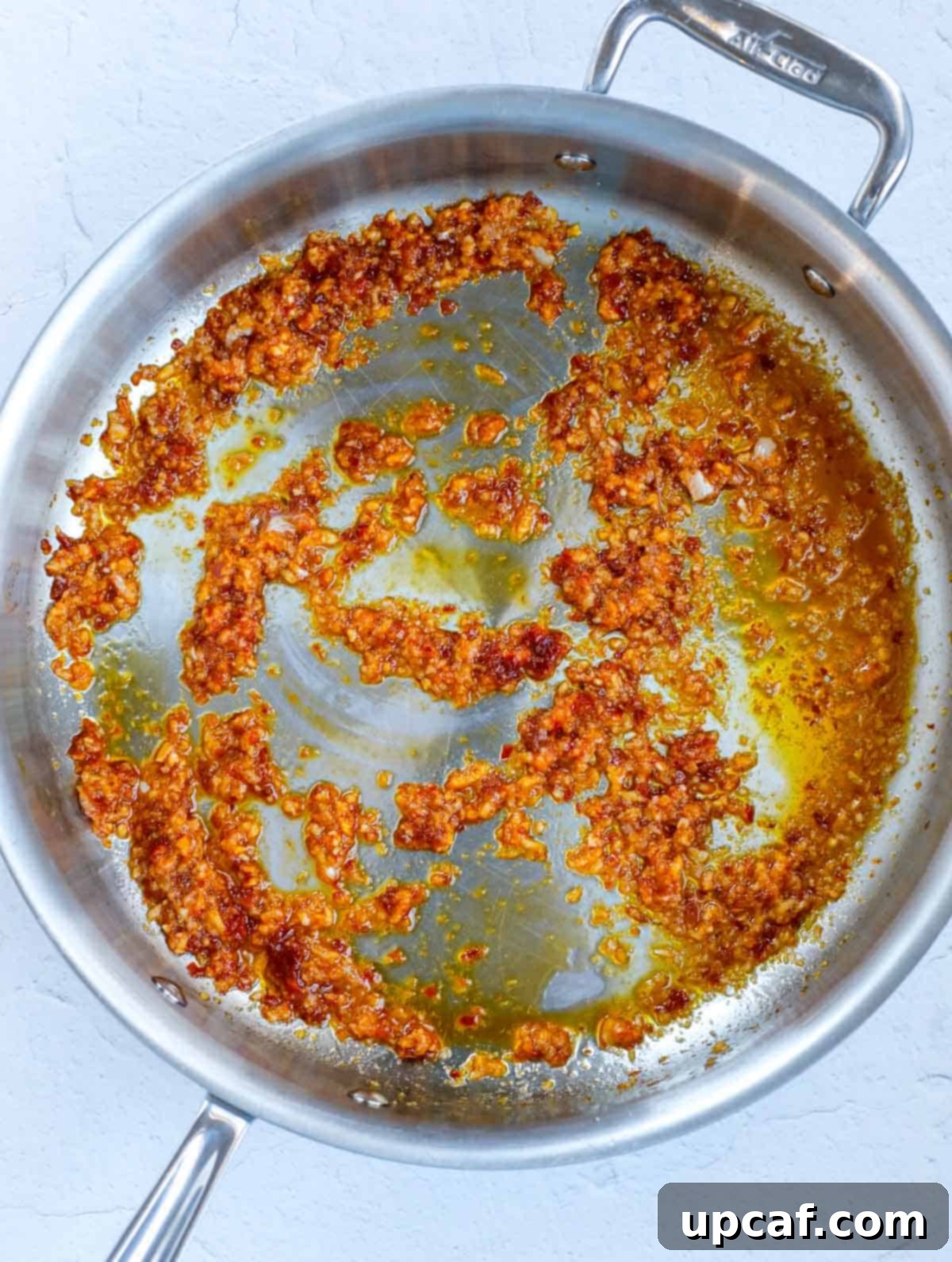 Minced garlic and red pepper paste sautéing in olive oil in a stainless steel pan.