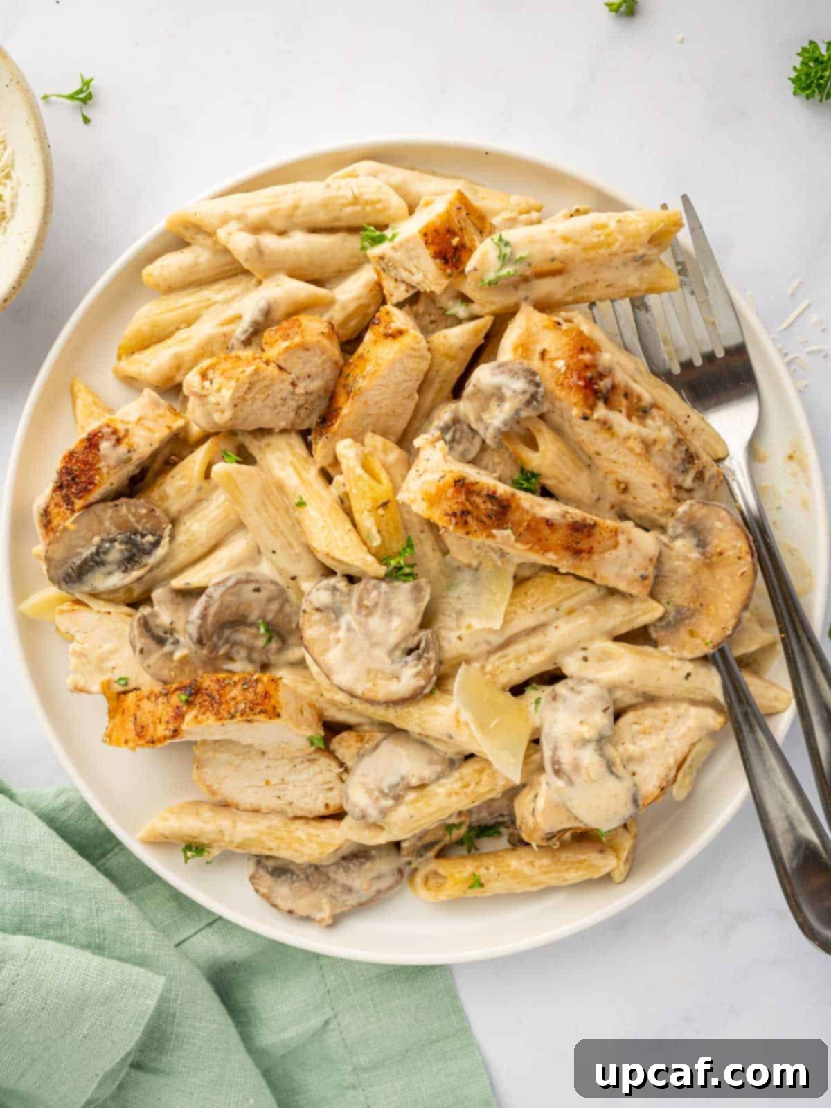 Creamy Garlic Parmesan Chicken Pasta 7 A fork lifts a savory bite of creamy chicken and mushroom pasta from a plate.