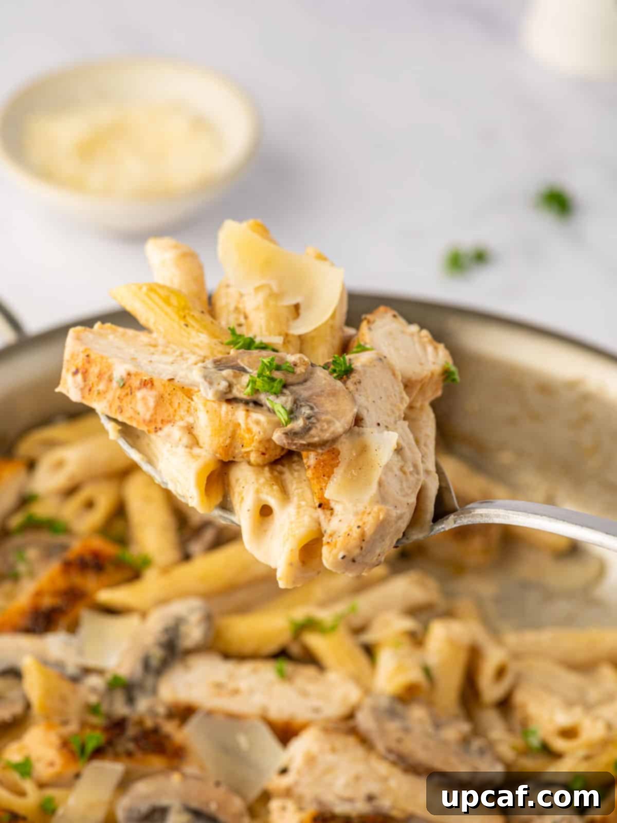 Creamy Garlic Parmesan Chicken Pasta 8 A spoon lifting a delightful bite of creamy chicken and mushroom pasta from a bowl.