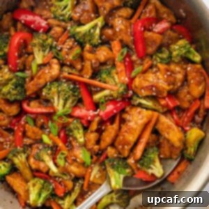 A spoon serve spicy hunan chicken from a skillet.