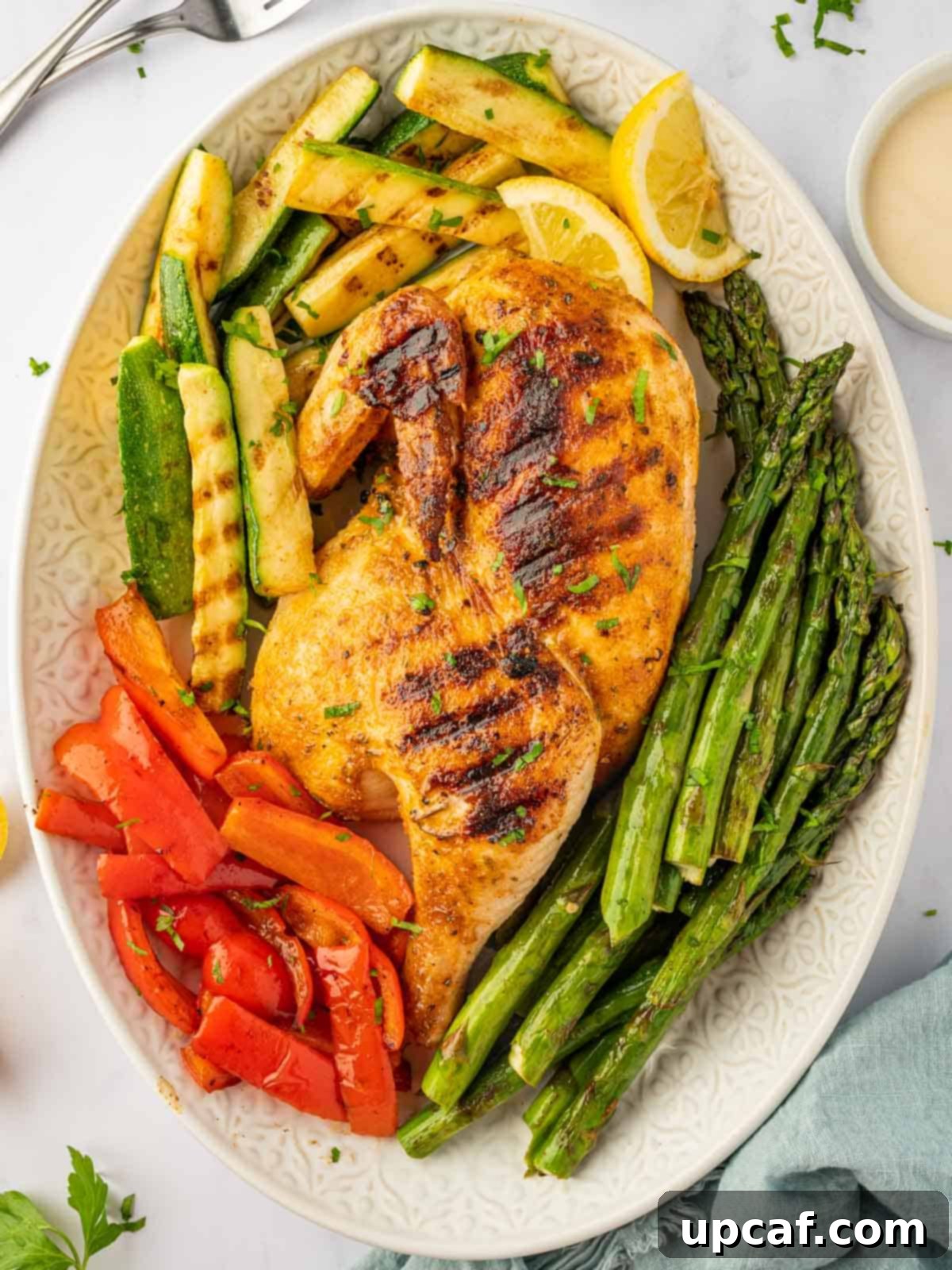 Beautifully grilled half chicken on a platter, garnished with fresh herbs and surrounded by vibrant grilled vegetables.