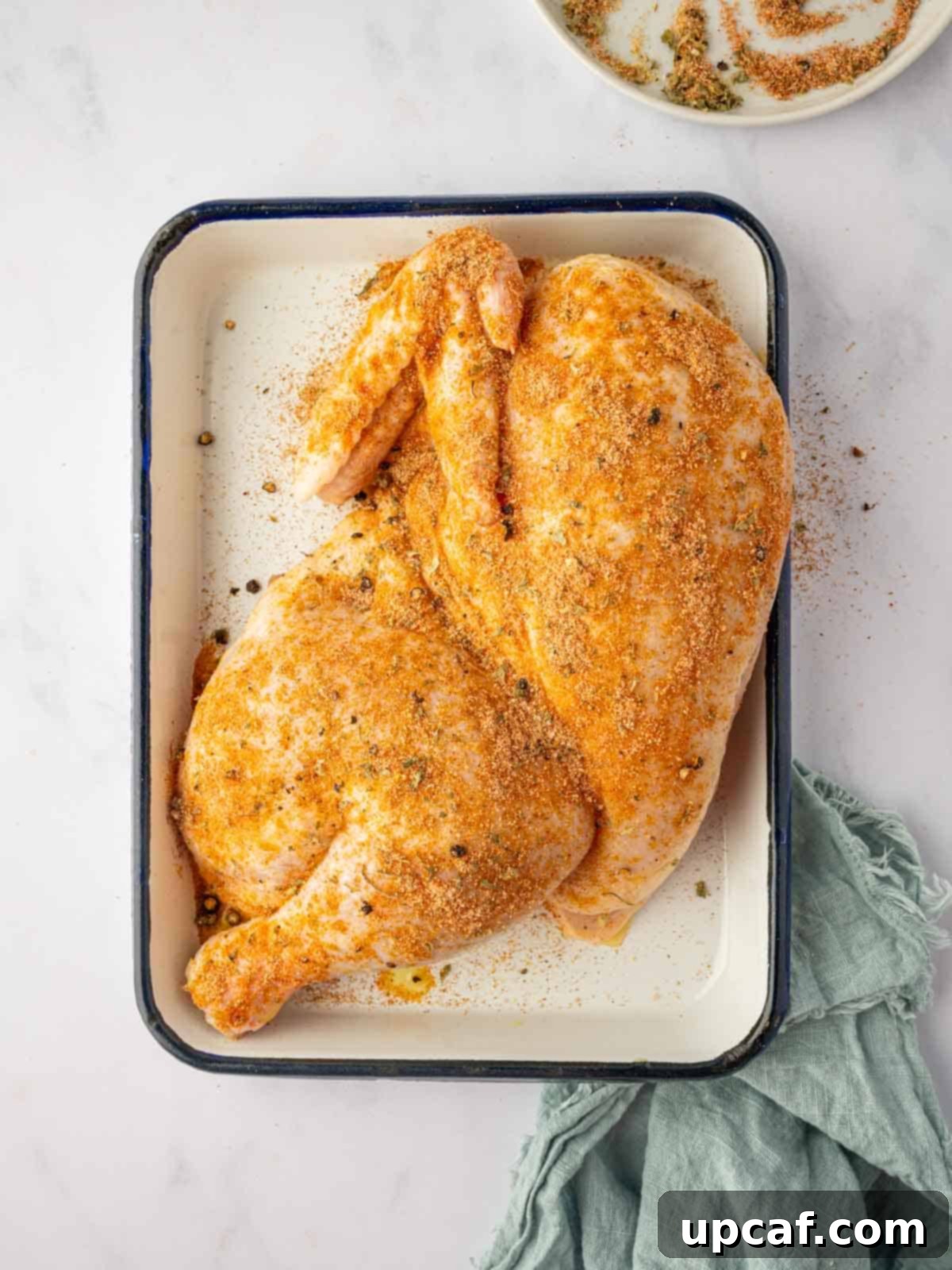 A half chicken generously coated with the flavorful herb and spice rub, ready for marination.