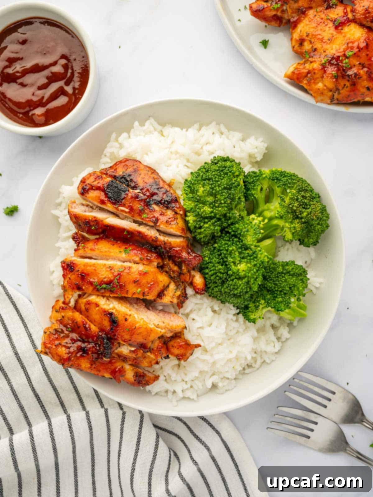 Perfectly Baked Boneless BBQ Chicken Thighs 2 Chicken thighs on a plate with broccoli and rice, ready to eat.