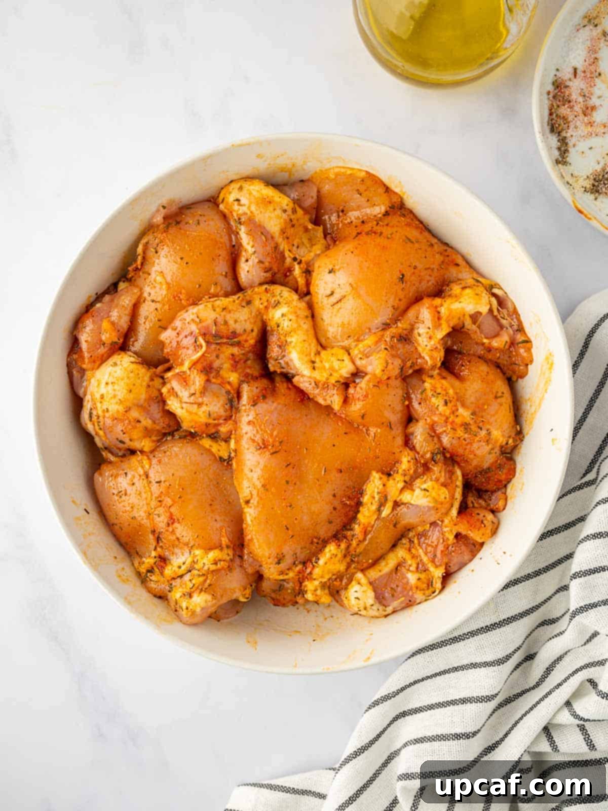 Perfectly Baked Boneless BBQ Chicken Thighs 4 Marinating chicken thighs in seasoning and olive oil in a bowl.