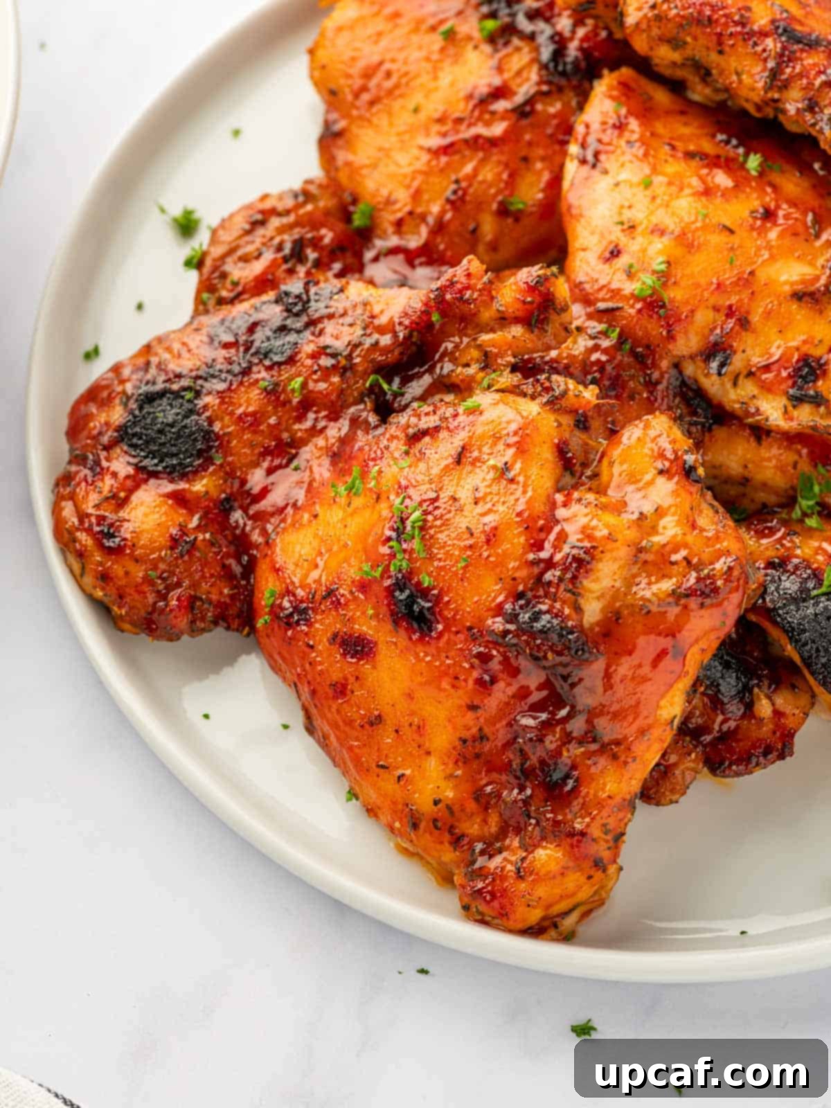 Perfectly Baked Boneless BBQ Chicken Thighs 8 Closeup of baked barbecue chicken thighs on a plate, garnished with parsley.