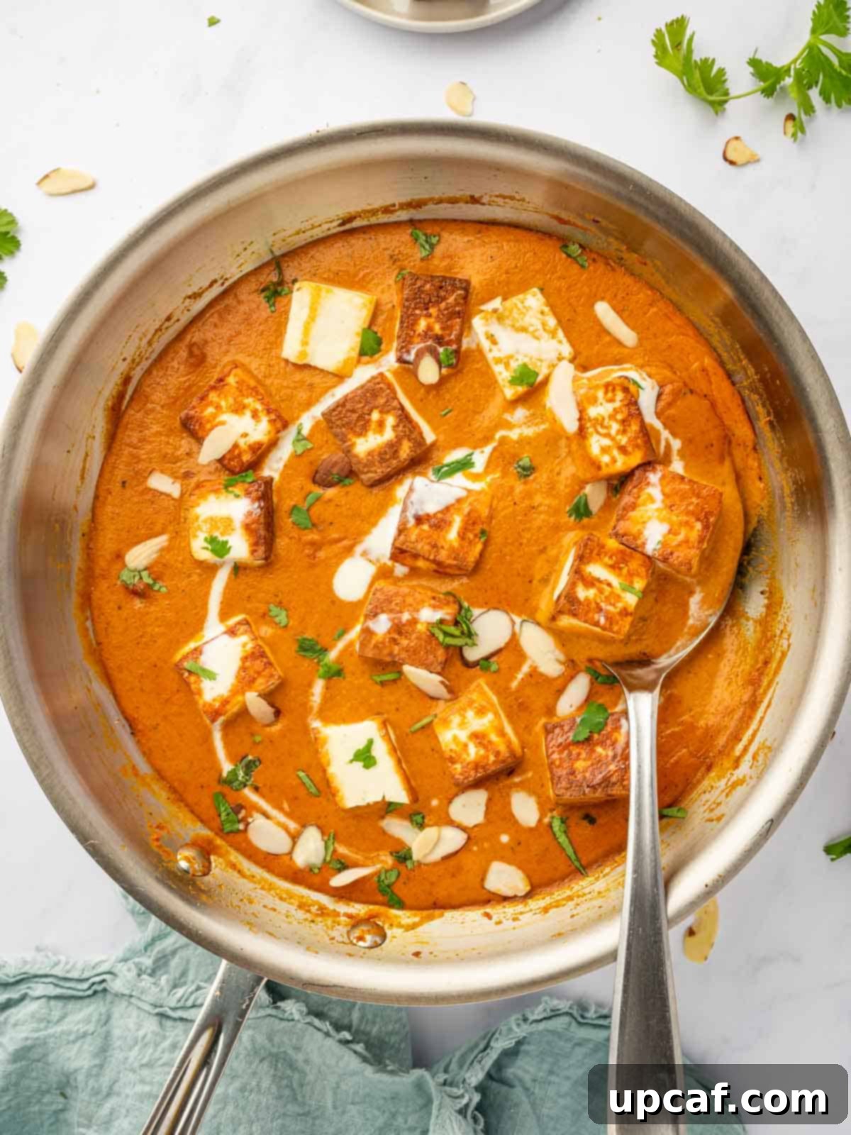 A spoon serves a helping of paneer pasanda, showcasing the rich, creamy texture and vibrant color of the curry.