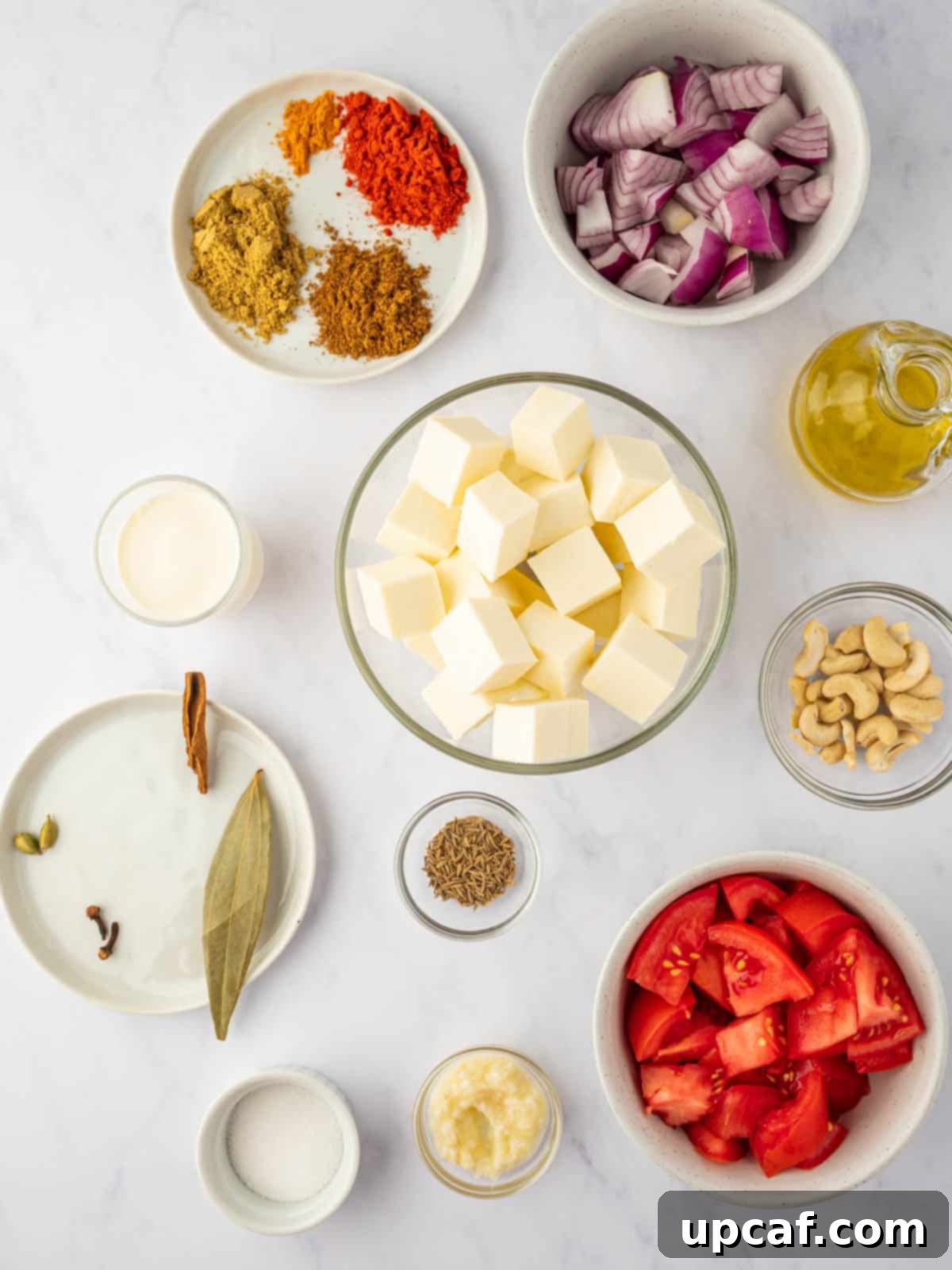A vibrant selection of ingredients laid out, including fresh tomatoes, red onions, paneer, cashews, and an array of aromatic spices, essential for crafting paneer pasanda.