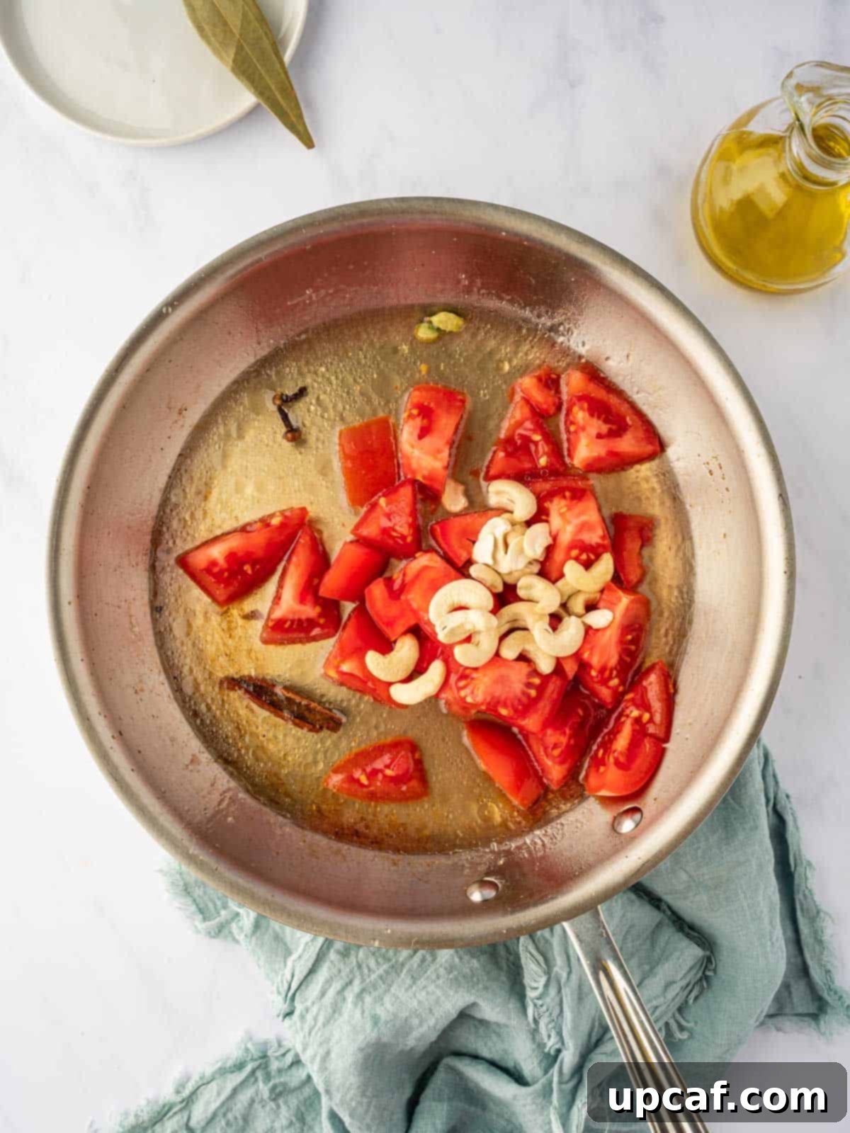 A close-up of sautéed tomatoes and cashews in a skillet, softening and simmering to create a flavorful sauce base.