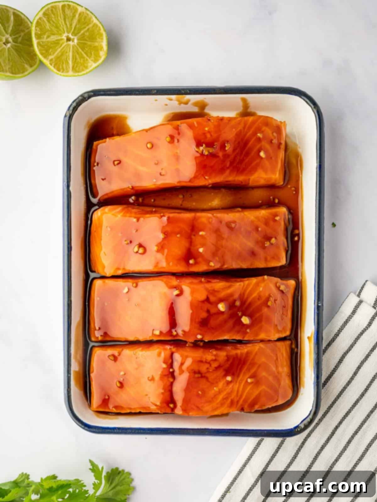 Sweet and Savory Teriyaki Salmon 5 Salmon fillets soaking in a rich, dark teriyaki marinade in a glass bowl, ready for grilling.