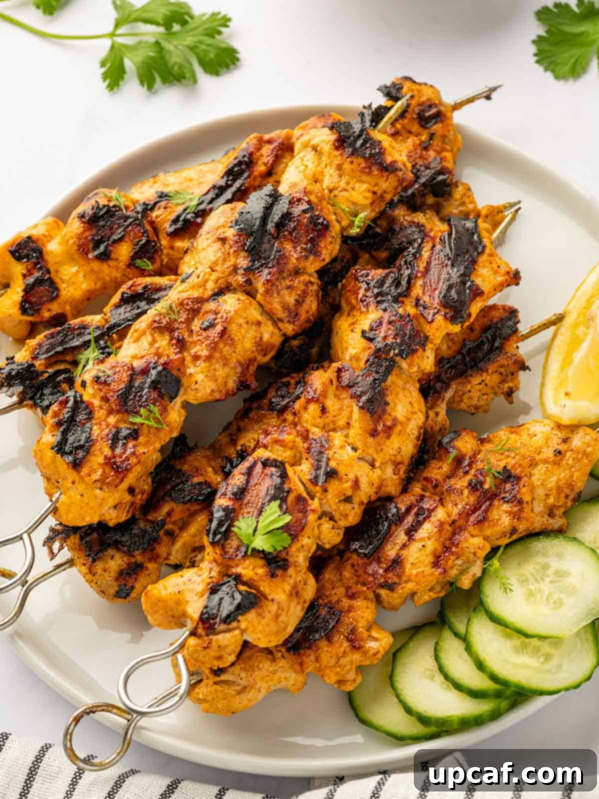 Beautifully grilled Tandoori chicken skewers served on a rustic platter with fresh cucumber slices and a vibrant green garnish.
