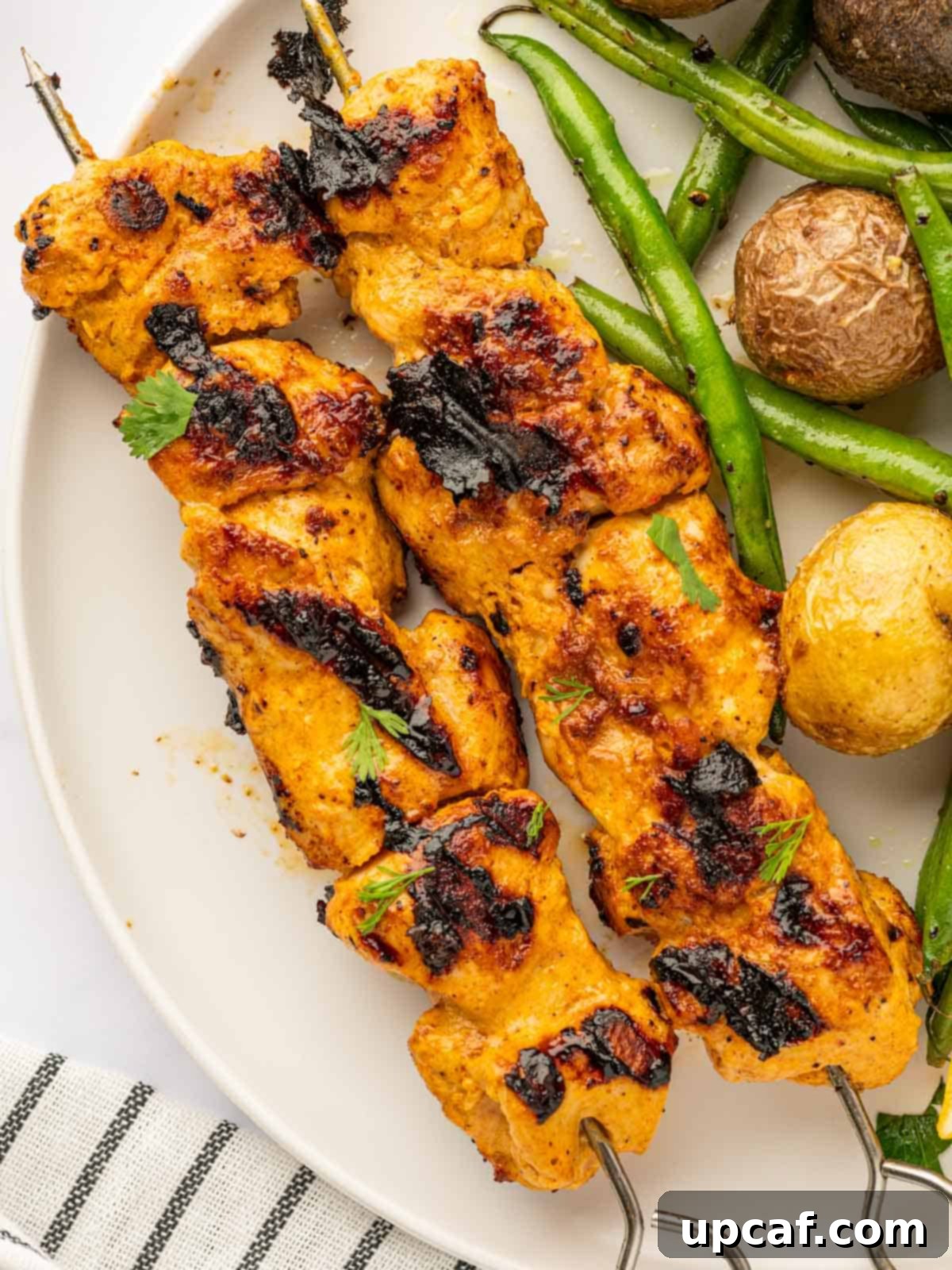 A complete meal featuring juicy Tandoori chicken skewers served on a plate with vibrant green beans and perfectly roasted potatoes.