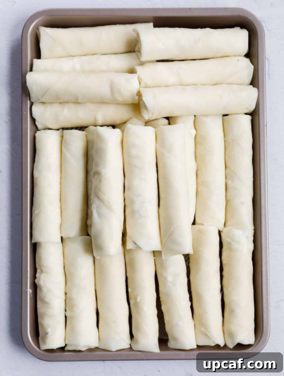 A bunch of cheese rolls neatly arranged in a pan, ready for frying.