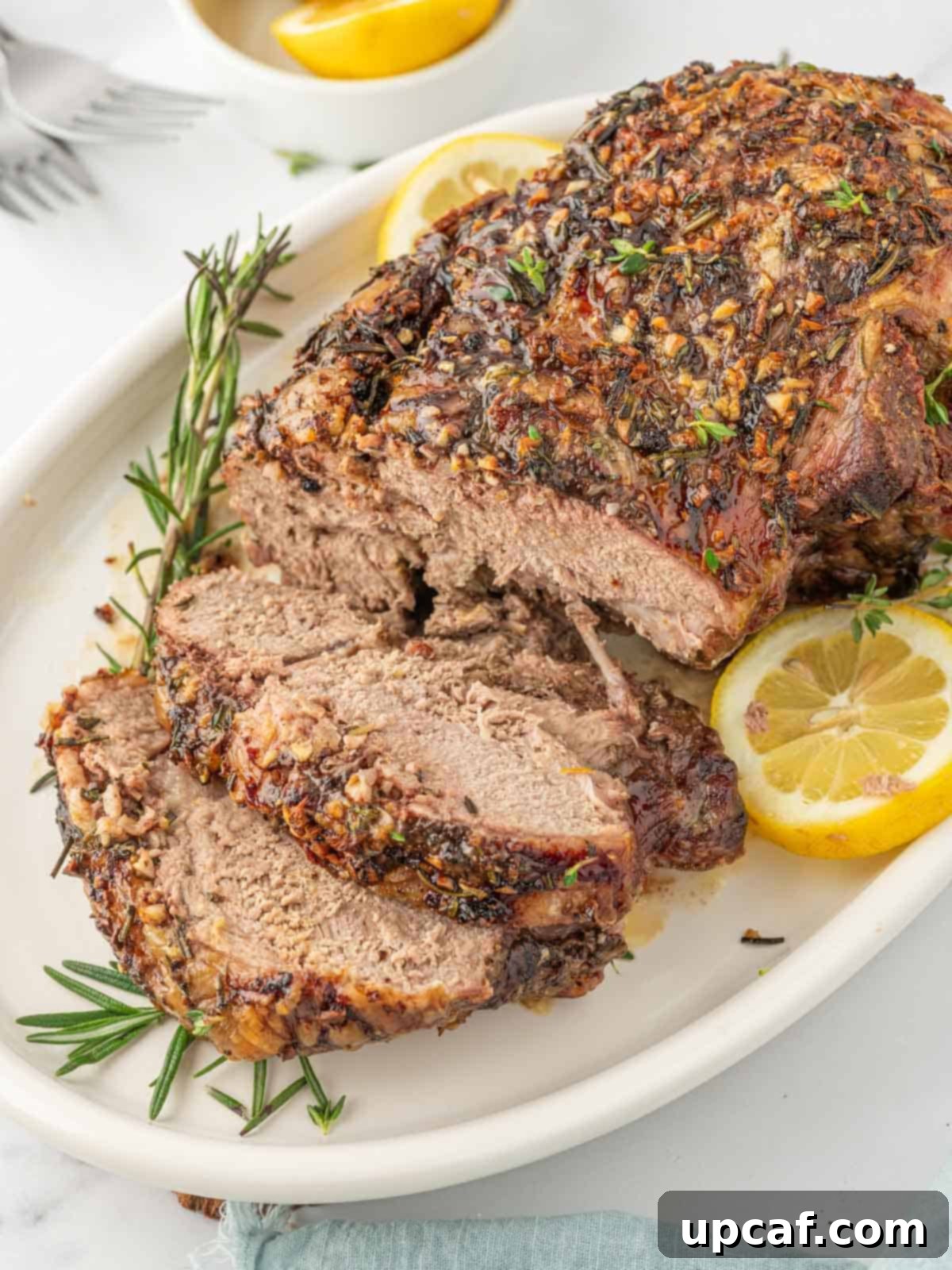 Rosemary Garlic Boneless Lamb Roast 2 Leg of lamb with slices cut garnished with lemon and rosemary.