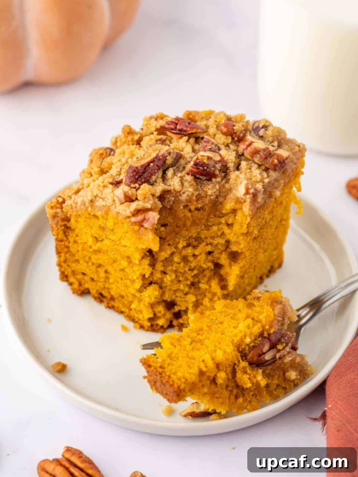 A fork taking a bite from a slice of pumpkin pecan coffee cake.