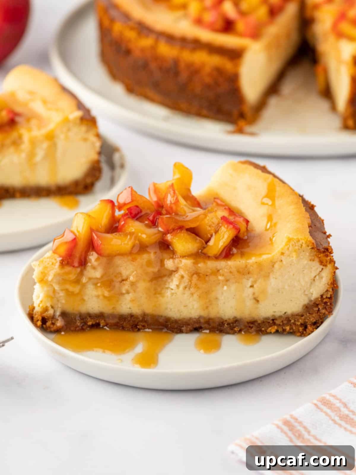 A perfectly cut slice of creamy cheesecake adorned with a generous layer of glistening cinnamon apple topping, resting on a white plate.