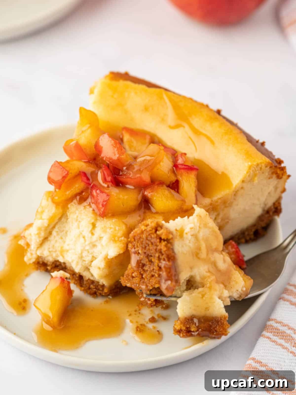 A fork taking a bite of creamy Cinnamon Apple Cheesecake, showing the smooth texture and the layer of spiced apples.