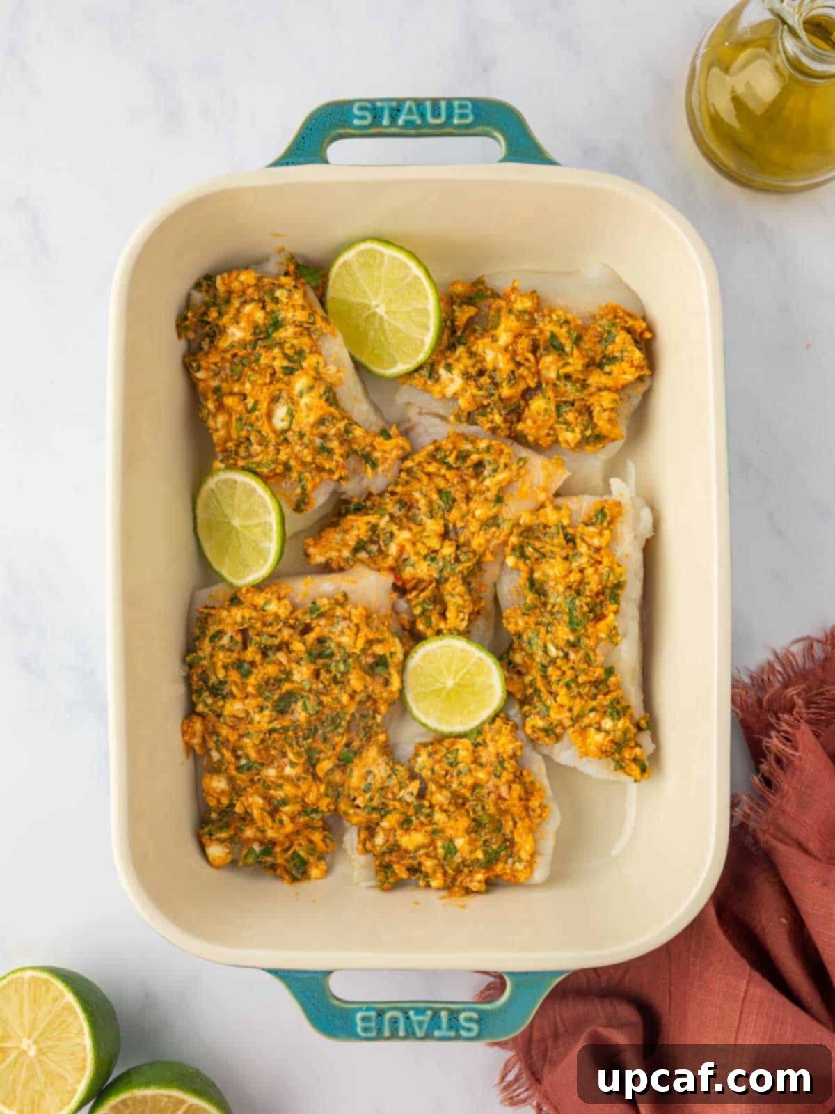 Cod fillets fully coated with the herb lime marinade, with lime slices arranged underneath, ready for baking.
