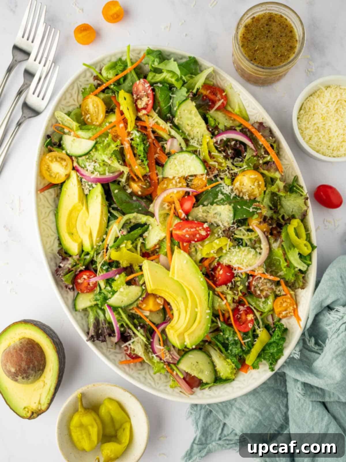 A beautifully tossed house salad topped with grated Parmesan cheese, showcasing vibrant greens, red tomatoes, and cucumber slices.