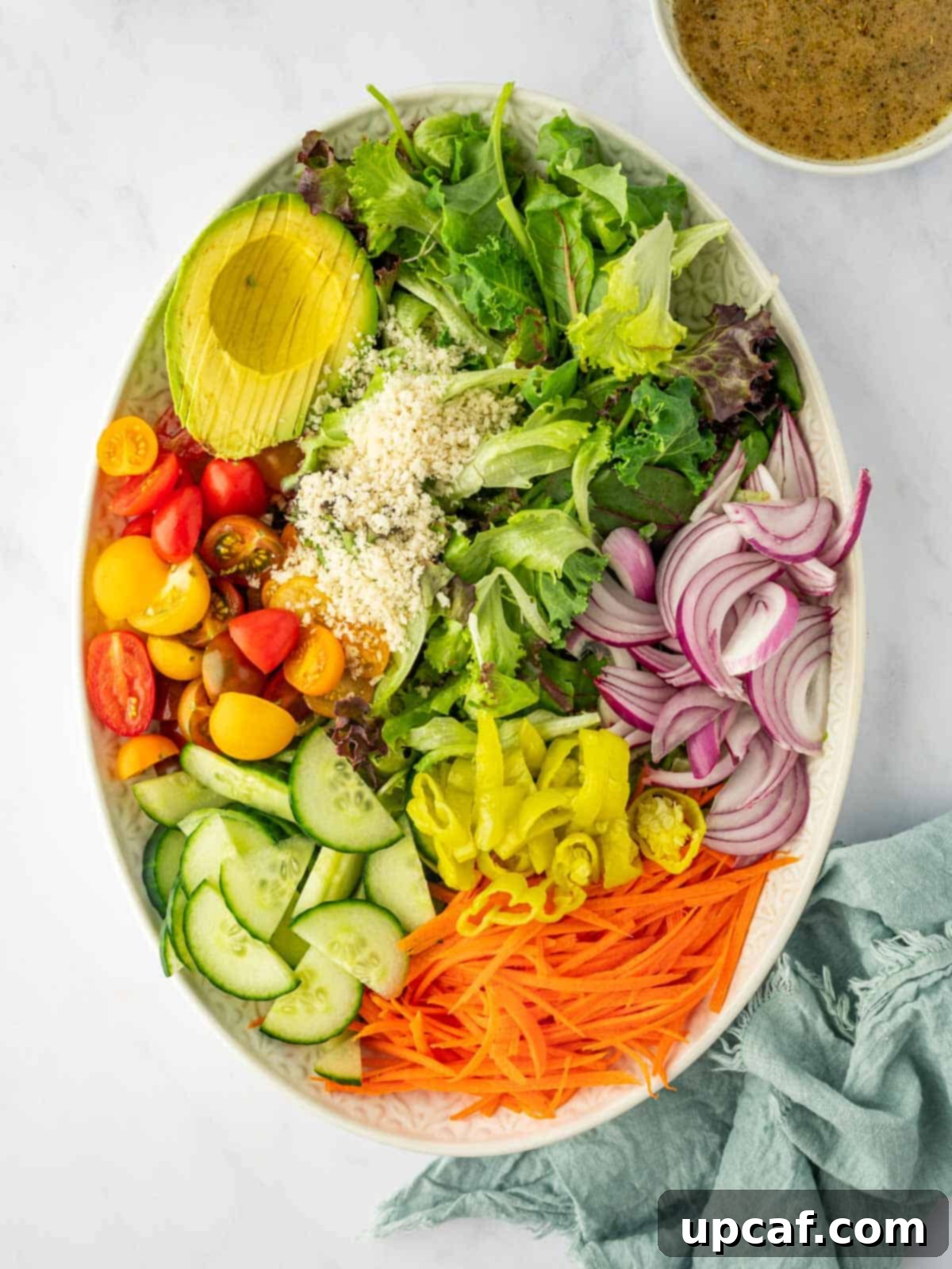 A vibrant assortment of freshly cut ingredients, including greens, tomatoes, cucumbers, onions, carrots, and avocados, laid out for a house salad.