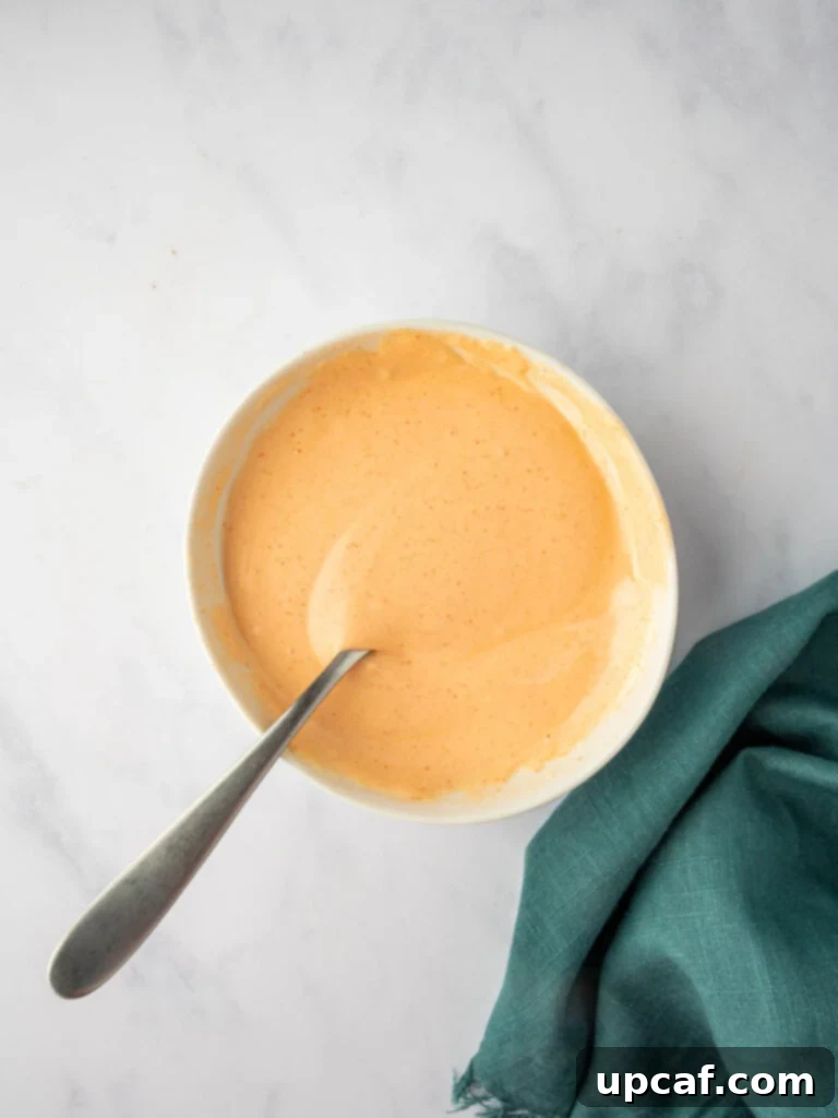 A bowl containing mayonnaise and sriracha, thoroughly mixed into a smooth, vibrant orange sauce.