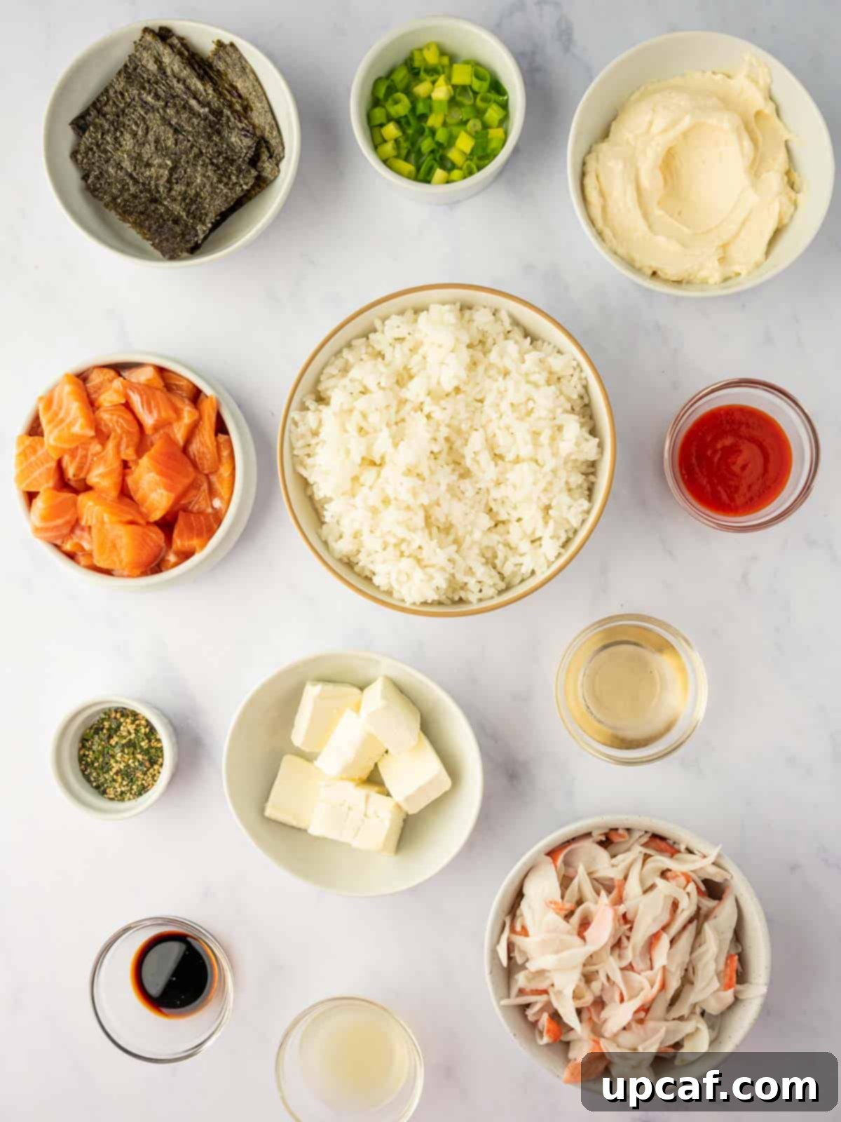 A collection of fresh ingredients for Salmon Sushi Bake, including salmon fillets, imitation crab, cream cheese, rice, avocado, and various sauces.