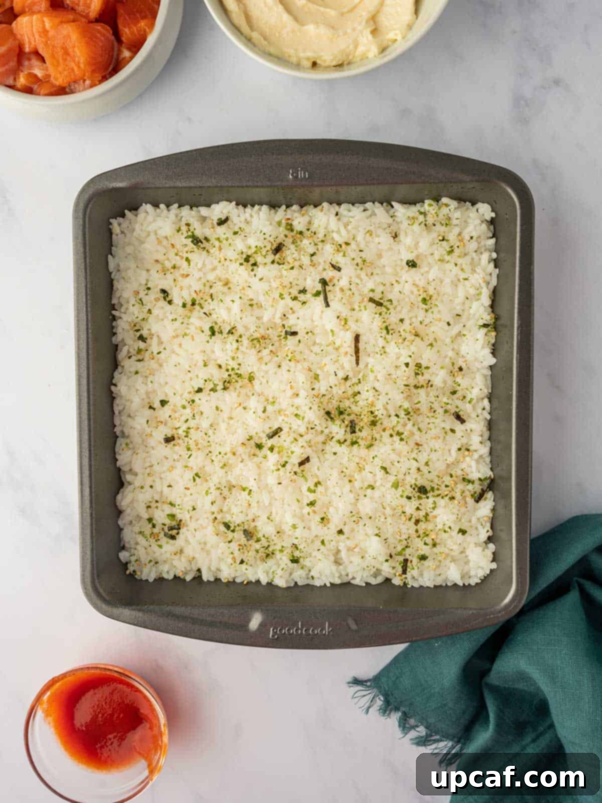 A uniform layer of seasoned sushi rice pressed firmly into the bottom of a square baking pan.